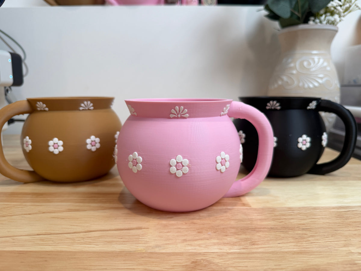 Pink Jarrito holder with raised white flowers alongside brown and black options