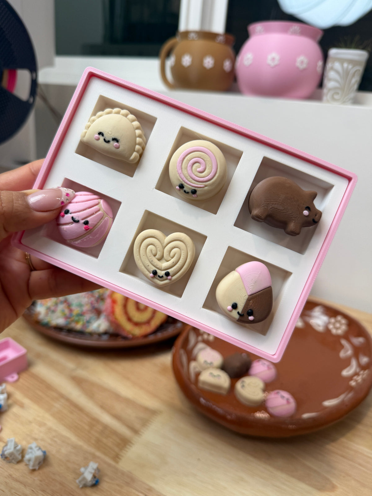 Handheld close-up of all six pan dulce clickers in the pink and white bakery box